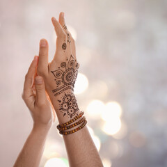 Woman with henna tattoo on hand against blurred lights, bokeh effect