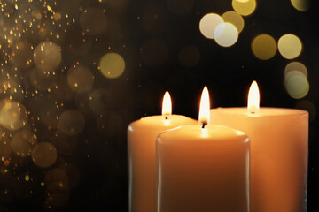 Wax candles burning on black background with blurred lights, closeup. Bokeh effect
