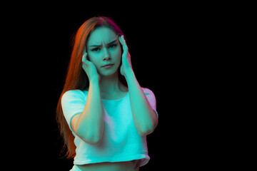 Portrait of emotive young girl in casual clothes posing isolated over black studio background in neon light