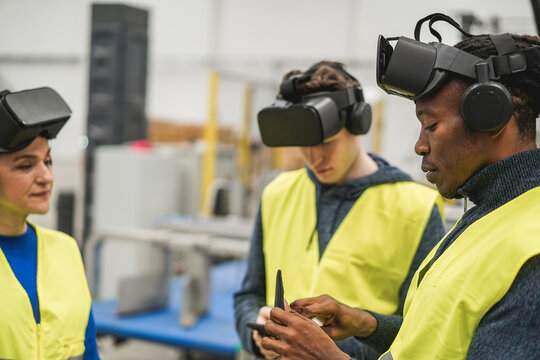 Multiethnic engineers using virtual reality glasses inside robotic factory - Focus on african man hand
