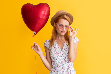 happy girl in eyeglasses hold love heart balloon on yellow background