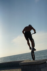 Trial biker performing on the rocks. Experienced biker does agility tricks on the beach in front of...