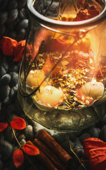 Close up of glass vase with water and floating candles at dark background with autumn leaves....