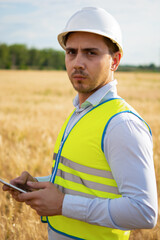 Fototapeta premium an engineer with a tablet in his hands stands in the middle of a green field, an agronomist in a field with wheat checks the harvest, summer day, smart farm, farming activities, eco products.