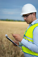 Fototapeta premium Agro engineer at the field inspection, the farmer stands in a wheat field with a folder in his hands and checks the harvest, the engineer stands in a field with wheat