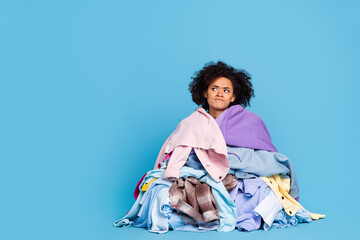 Photo of depressed doubtful young woman covered big stack clothes looking empty space isolated blue color background