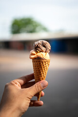 Chocolate ice cream scoop in waffle cone, holding by human hand with blurred background. Food object photo.