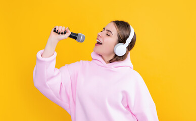 glad young girl in headphones with microphone on yellow background