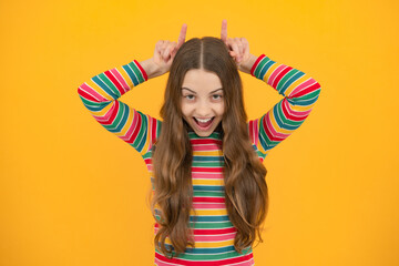 Excited face, cheerful emotions of teenager girl. Beautiful little girl doing funny gesture with finger over head as bull horns.