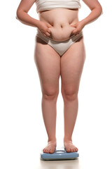 Fat belly woman standing on a scale and squeezing a fat roll on her belly on white background