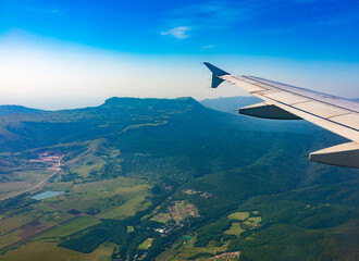 Obraz premium View of airplane wing, blue skies and green land during landing. Airplane window view.