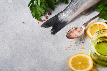 Fresh fish. Sea Bass raw with salt, pepper, parsley, olive oil and lemon on cutting board on light gray concrete rustic background. Food cooking background. Top view, copy space.