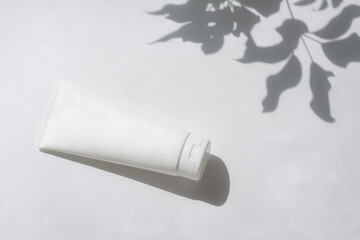Cosmetic bottle with leaf shadow on white wall background