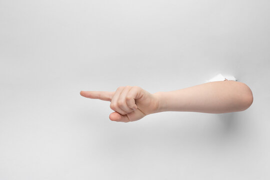 child hand pointing the forefinger to the left through hole in white paper with torn edges, concept of attention with copy space