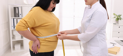 Nutritionist measuring overweight woman's waist with tape in clinic. Banner design
