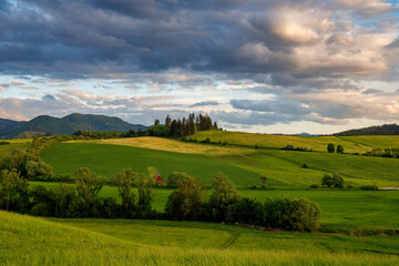 Fototapeta na wymiar Spring rural landscape with dramatic sky at sunset. Meadows on the hillside of the Little Fatra Mountains in Slovakia, Europe.