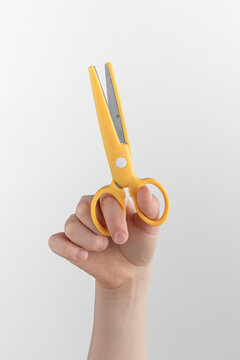 Child hand holding yellow scissors for left-handers. white and gray background with copy space