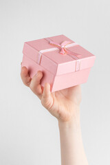 Child hand holding gift box with pink bow. white and gray background with copy space
