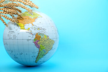 Fototapeta premium Globe with wheat spikelets on turquoise background, space for text. Hunger crisis concept