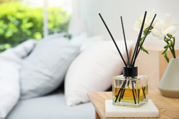 Reed diffuser and vase with bouquet on wooden nightstand in bedroom. Space for text - obrazy, fototapety, plakaty