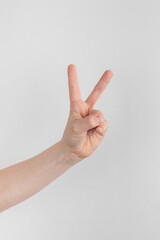 child hand counting and showing two finger up against white and gray background. peace gesture or victory, V sign