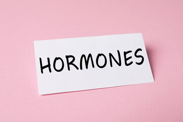 Sheet of paper with word Hormones on pink background