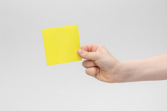 child hand holding a square yellow blank reminder or paper notes above a white and gray background, copy space