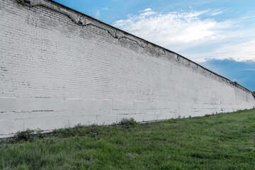 Long spacious empty old white colored brick wall structured on green grass against blue sky