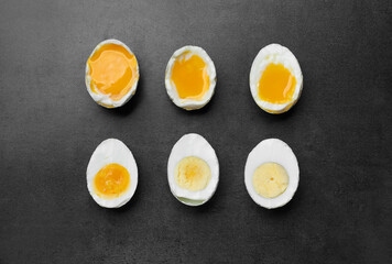 Different readiness stages of boiled chicken eggs on dark grey table, flat lay