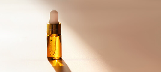 Cosmetic amber glass dropper bottle with oil, serum or fruit peeling in the sunlight on beige...
