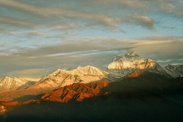 Fototapeta na wymiar Warm pink and orange dramatic sunrise light over Annapurna mountain range with beautiful clouds, view from Poon hill in Himalayas, Nepal