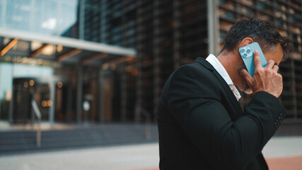 Middle-aged businessman with neat beard in office clothes uses mobile phone. Successful man emotionally talking on smartphone. Disappointment, trouble