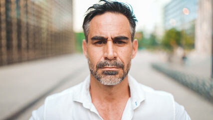 Close-up Businessman mature with neat beard wearing white shirt looks turns his head at the camera in the financial district in the city