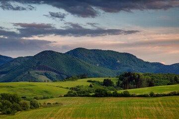 Spring rural landscape with dramatic sky at sunset. Meadows on the hillside of the Little Fatra Mountains in Slovakia, Europe.