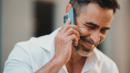 Close-up mature businessman with neat beard uses mobile phone sits on bench in the financial...