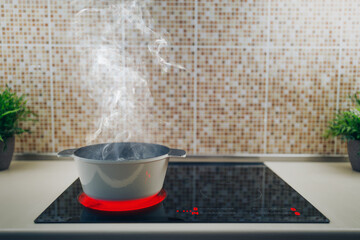 white boiling pot with hot steam on electrical induction cooktop