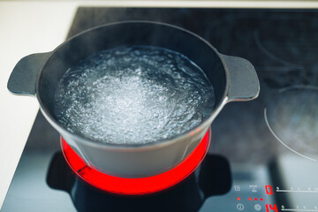 white boiling pot with hot steam on electrical induction cooktop