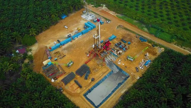 Cinematic Drone Shot of Onshore Drilling and Workover Rig structure and Rig equipment for oil exploration and exploitation in the middle of jungle surrounded by palm oil trees during sunset time.