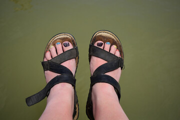 Füße in Sandalen mit lackierten Zehennägeln über Wasser, natürlich