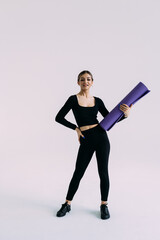 Beautiful smiling young woman in sportswear holding a yoga mat on white background. Healthy lifestyle concept. Fitness and yoga concept.