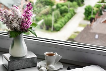 Still life with lilac flowers in a white vase on the windowsill. Notepad for notes and a cup of coffee, cozy home business planning