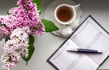 Top view flat lay with lilac flowers in a white vase on a windowsill. Notepad for notes and a cup of coffee, cozy home business planning