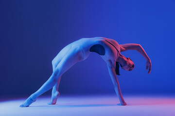 Naklejka na ściany i meble Portrait of young sportive girl doing stretching exercises isolated over blue studio background in neon light. Bridge position