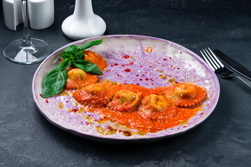 Ravioli with tomato sauce garnished with parmesan cheese and basil on table