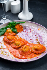 Ravioli with tomato sauce garnished with parmesan cheese and basil on table