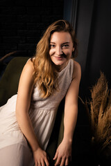 A young woman in a dress with long hair smiles and looks at the camera in a dark room.