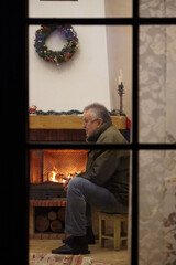 elderly man sitting in front of fireplace. View through window....