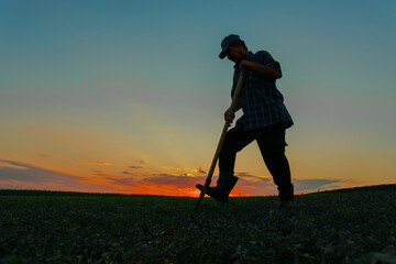 the silhouette of a peasant man working digging on agricultural land at sunset against the...