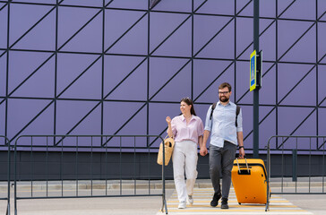 Couple of tourists travelers with tickets and an orange plastic orange suitcase cross a pedestrian crossing heading for a boarding. travel summer vacation voyage 
