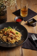 a traditional dish of Italian pasta cuisine. restaurant serving. black plate. wooden table.